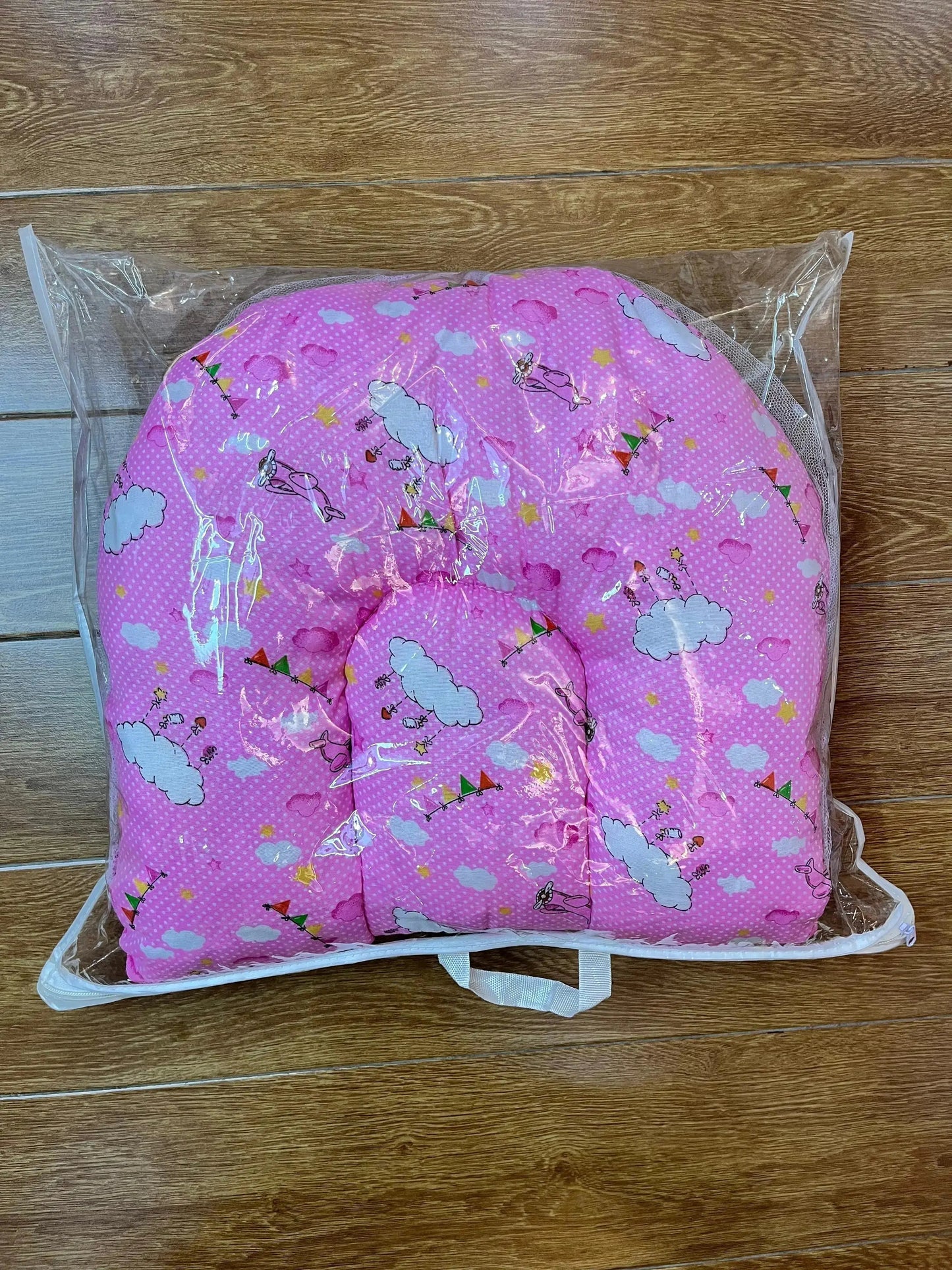 Pink baby pillow with cartoon cloud print in clear plastic packaging on wooden floor