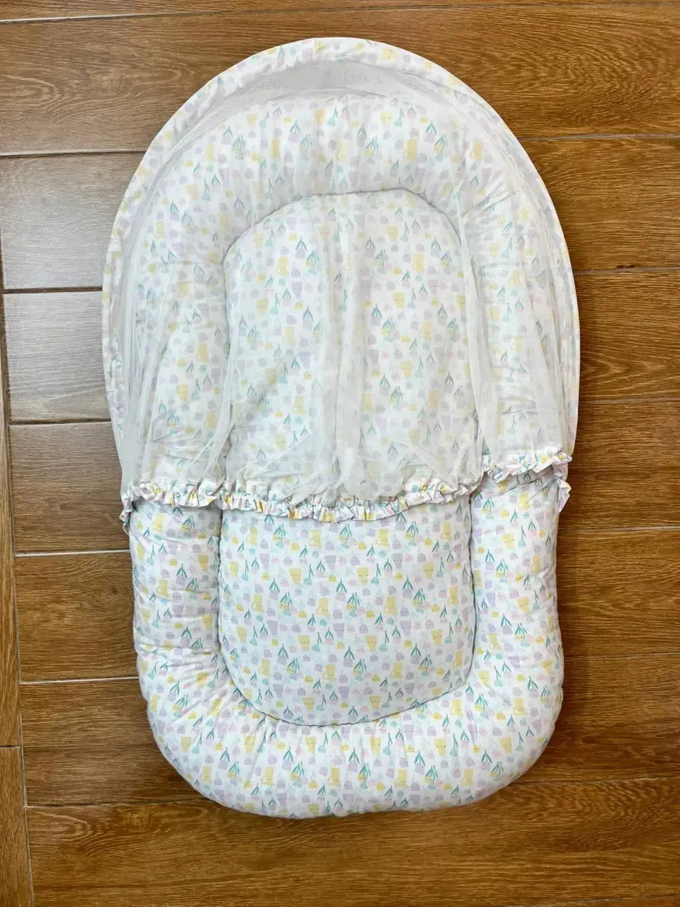 Soft baby nest with pastel house pattern on wooden floor, Little Flower brand