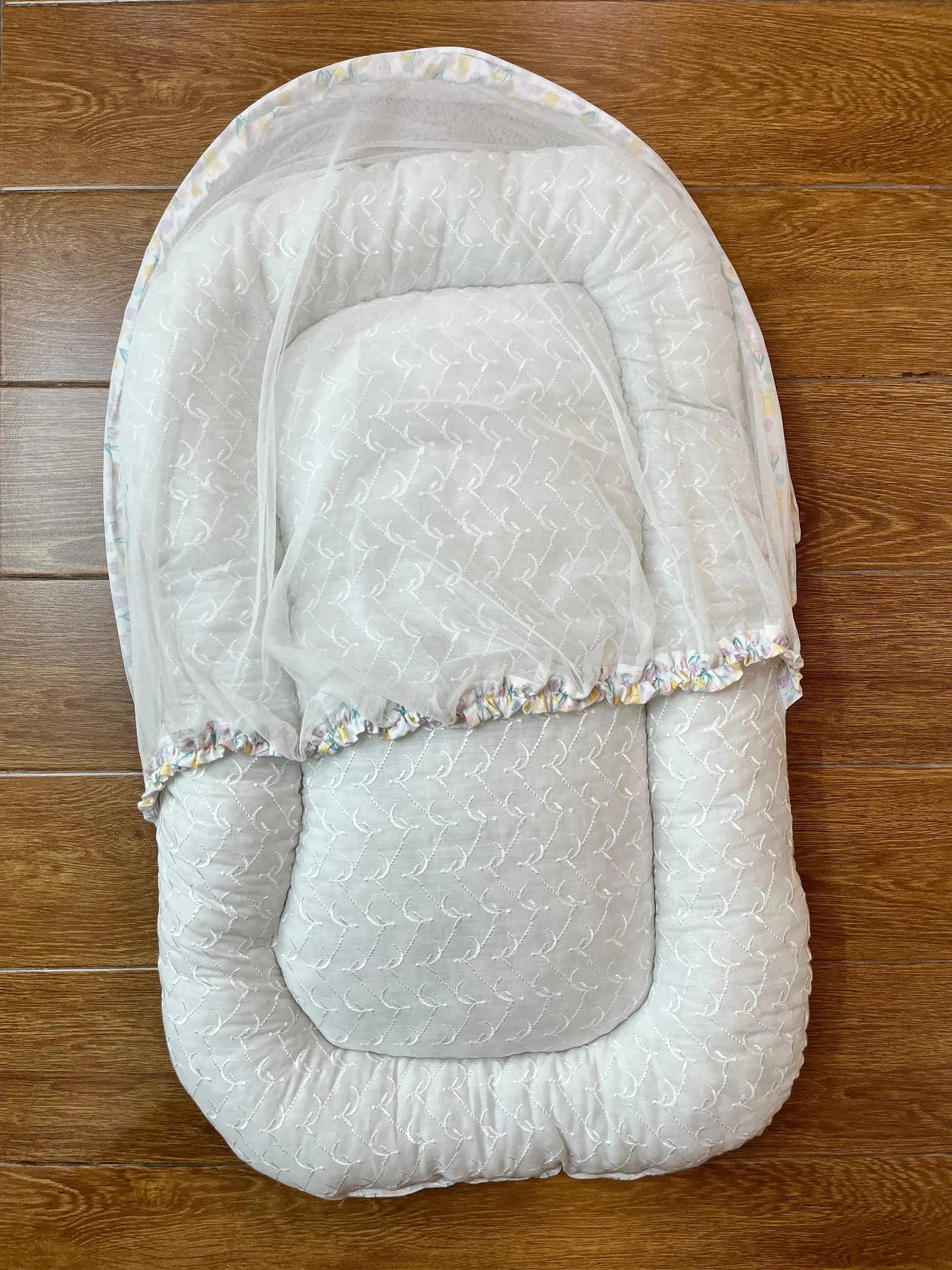 White quilted baby nest with sheer net cover on wooden floor, Little Flower store